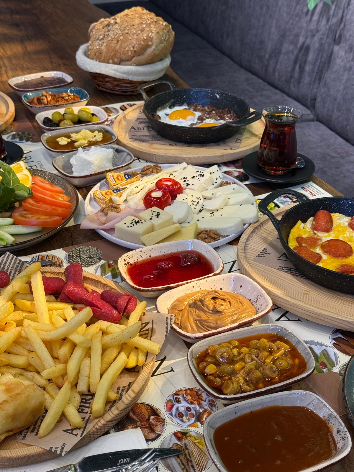 Çorlu Arı Fırın Pastaneleri'nde peynir tabağı, simit, sahanda yumurta ve patates kızartması ile dolu zengin serpme kahvaltı sofrası. – Arı Fırın Çorlu