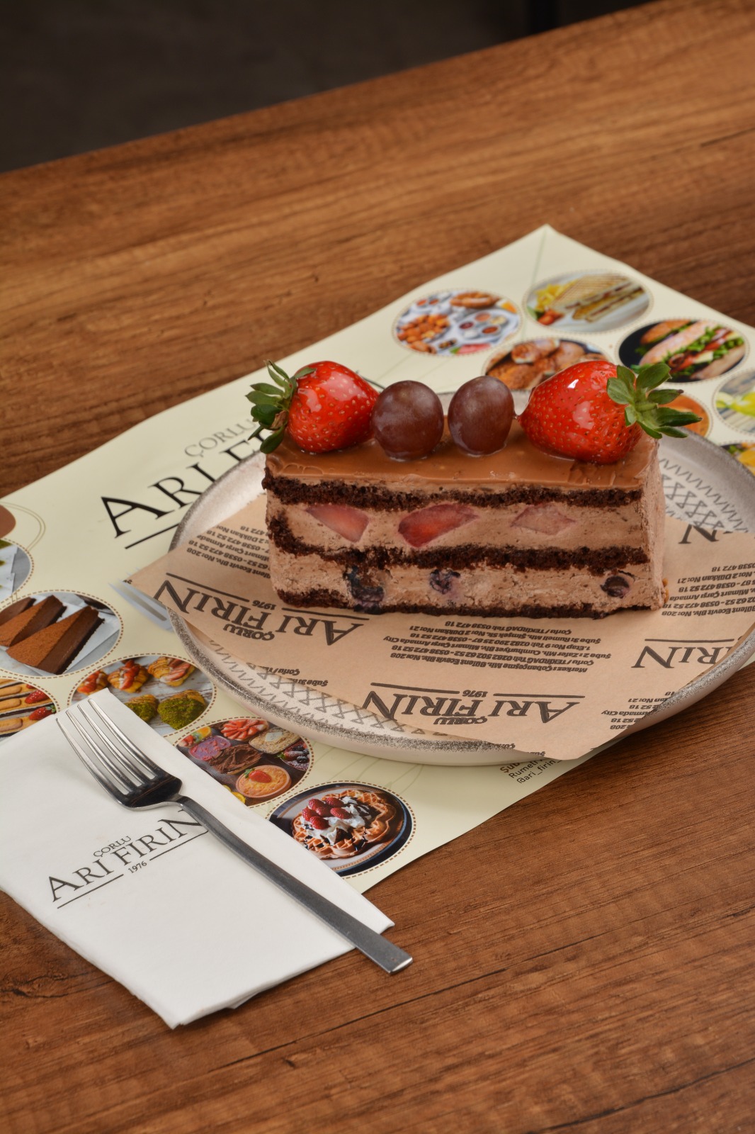 Kakaolu pandispanya arasına meyve parçacıklı krema dolgulu, üzeri taze çilek ve üzümle süslenmiş çikolatalı dilim pasta. – Arı Fırın Çorlu